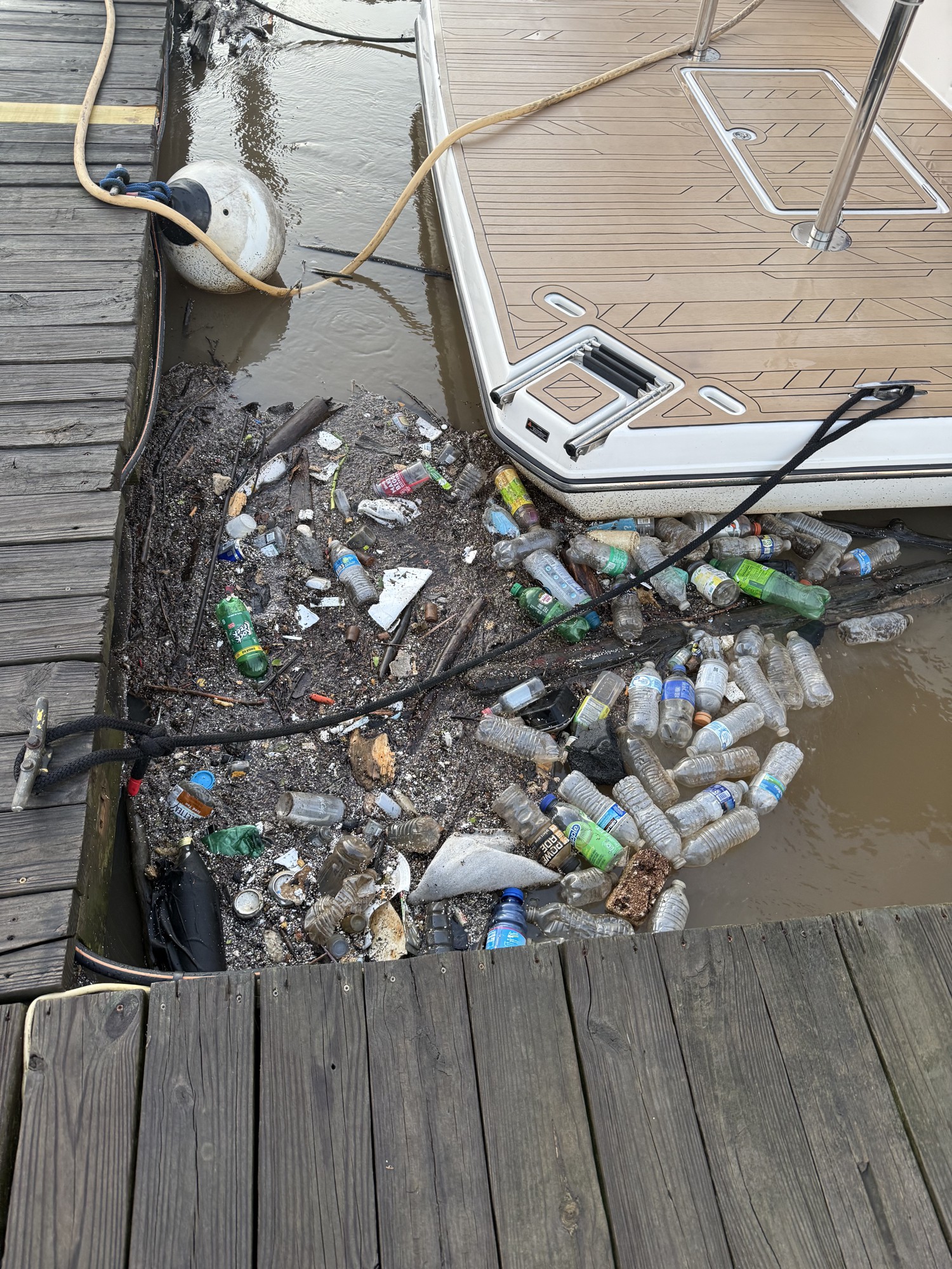 A raft of plastic bottles and debris packed between a boat’s stern and the dock at the club.