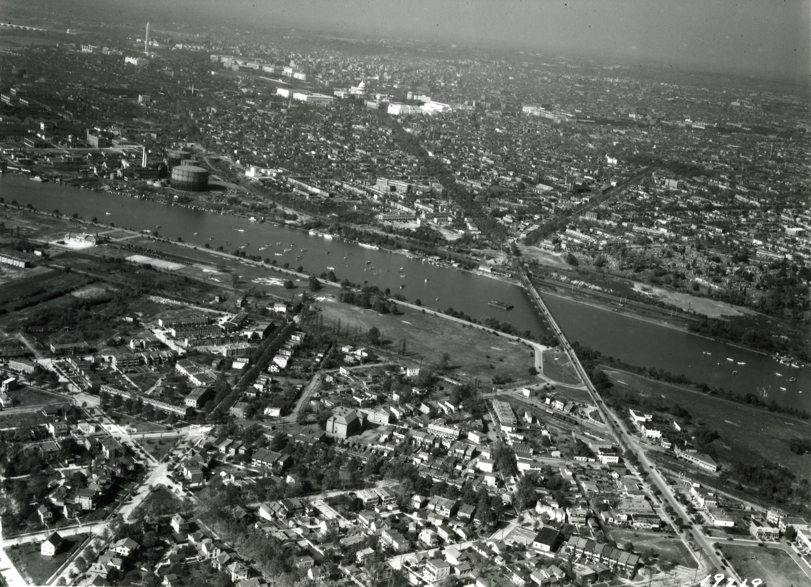Aerial view of the Anacostia River and Washington, DC in 1932, a large cylindrical gasworks storage tank standing on the near riverbank, the Capitol and Washington Monument on the horizon.