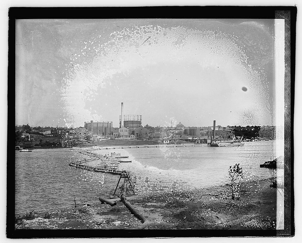 The Anacostia flats in 1921, a dredge pipeline along the reclaimed shore in the foreground and the riverside gasworks with its great gas-holder tanks beyond.