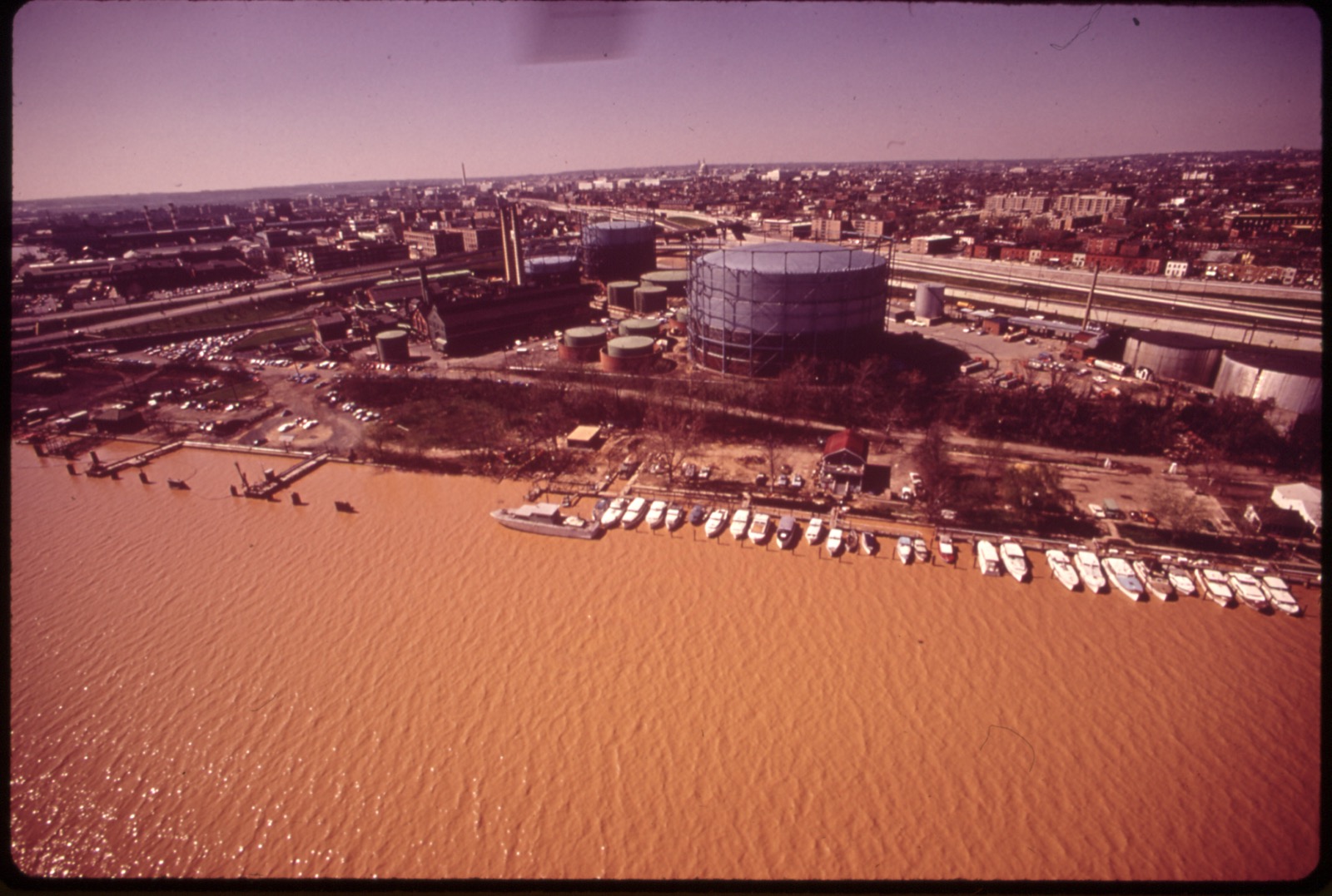 A 1973 color aerial of the Eastern Power Boat Club, its boats along the docks on a rust-orange, polluted Anacostia River.