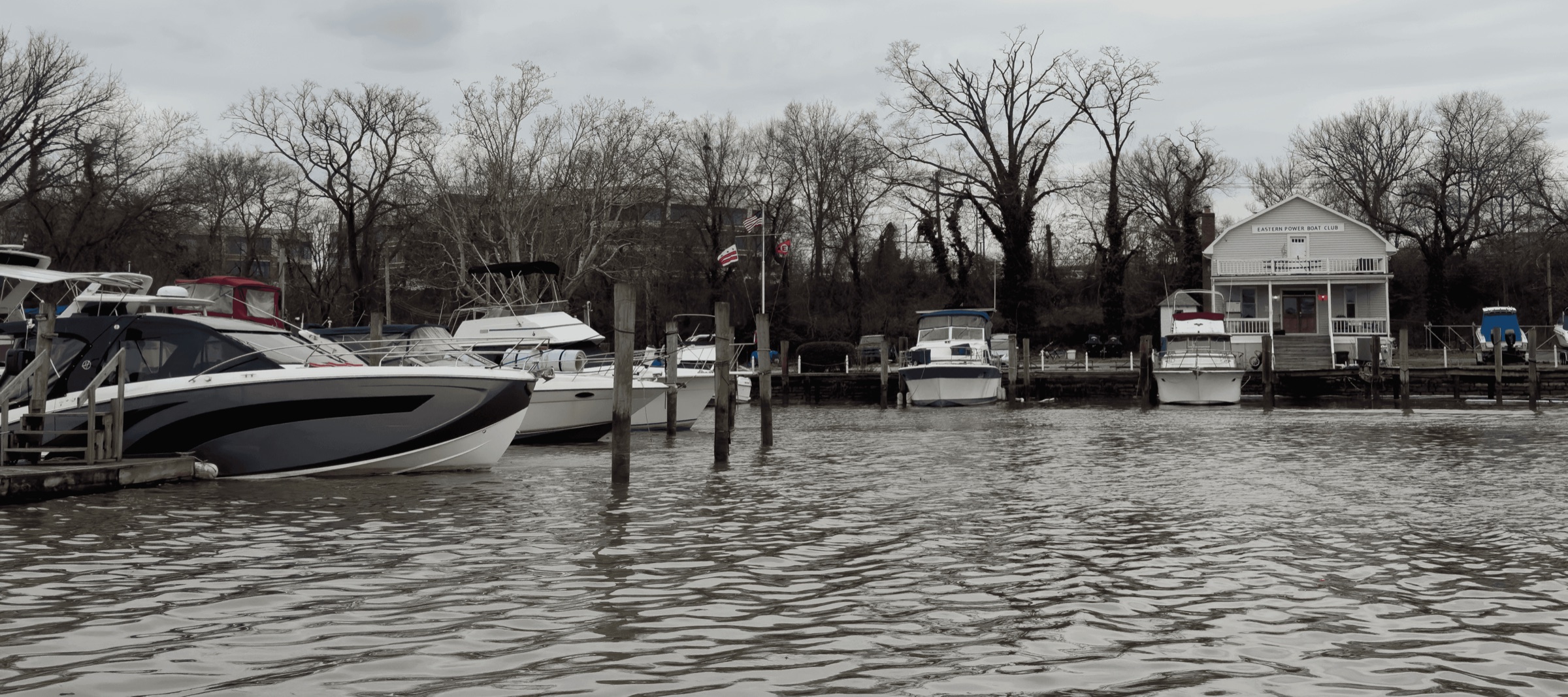 The Eastern Power Boat Club clubhouse seen from the Anacostia, boats along the docks and the U.S. and District of Columbia flags and the club burgee flying.