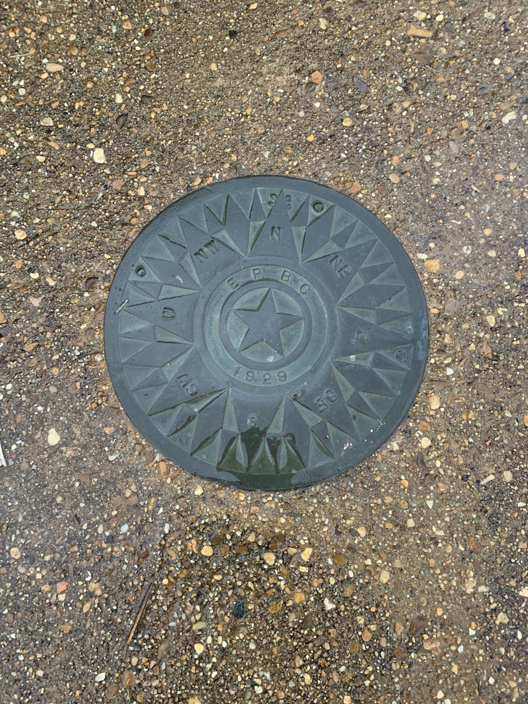 A cast metal compass rose lettered E.P.B.C. and dated 1929, set into the ground at the foot of the clubhouse stairs.
