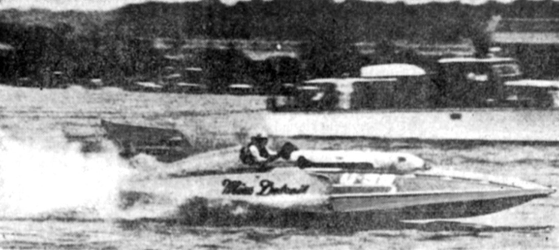 The unlimited hydroplane Miss Detroit at speed on the Potomac during the 1960 President’s Cup, throwing spray, with cars and spectators lining the shore.
